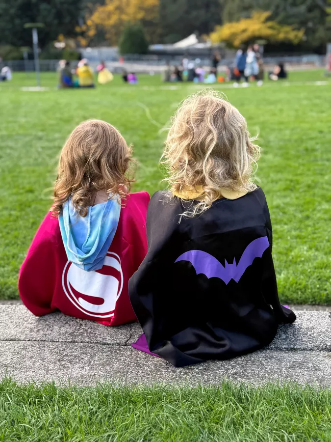 two young children dressed as superheroes sit on the lawn overlooking elephantlands